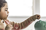 little girl putting money in piggy bank