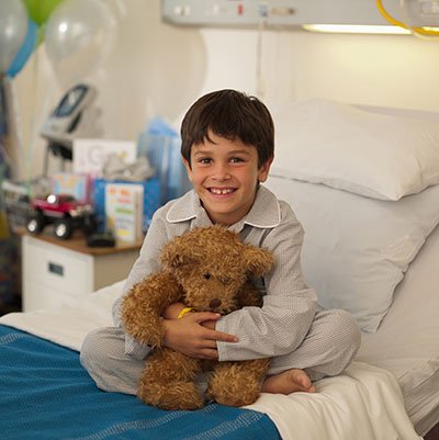 Child sitting in bed with teddy bear