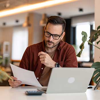 man with paperwork at laptop computer