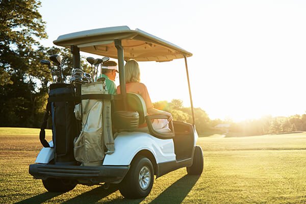 couple driving a golf cart across a green