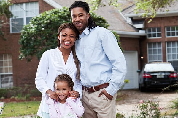 family with little girl standing on lawn in front of their house