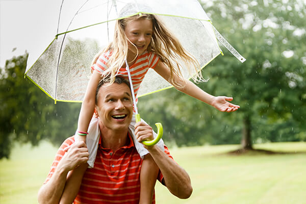 daughter on fathers shoulders holding umbrella in the rain.